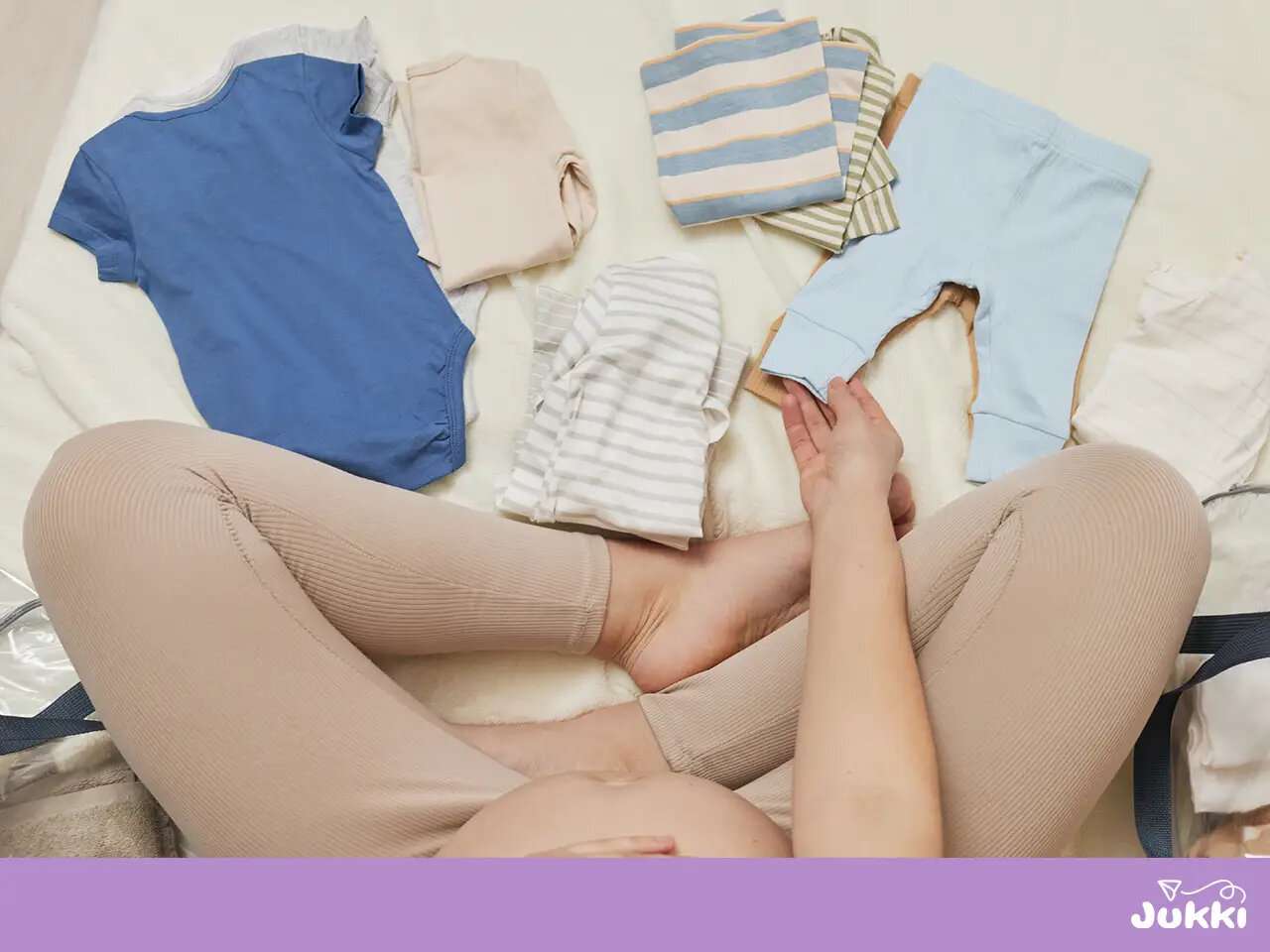 Egy kismama a földön ülve, összehajtogatott színes babaruhákat és bodykat rendszerez a szülés előtt.